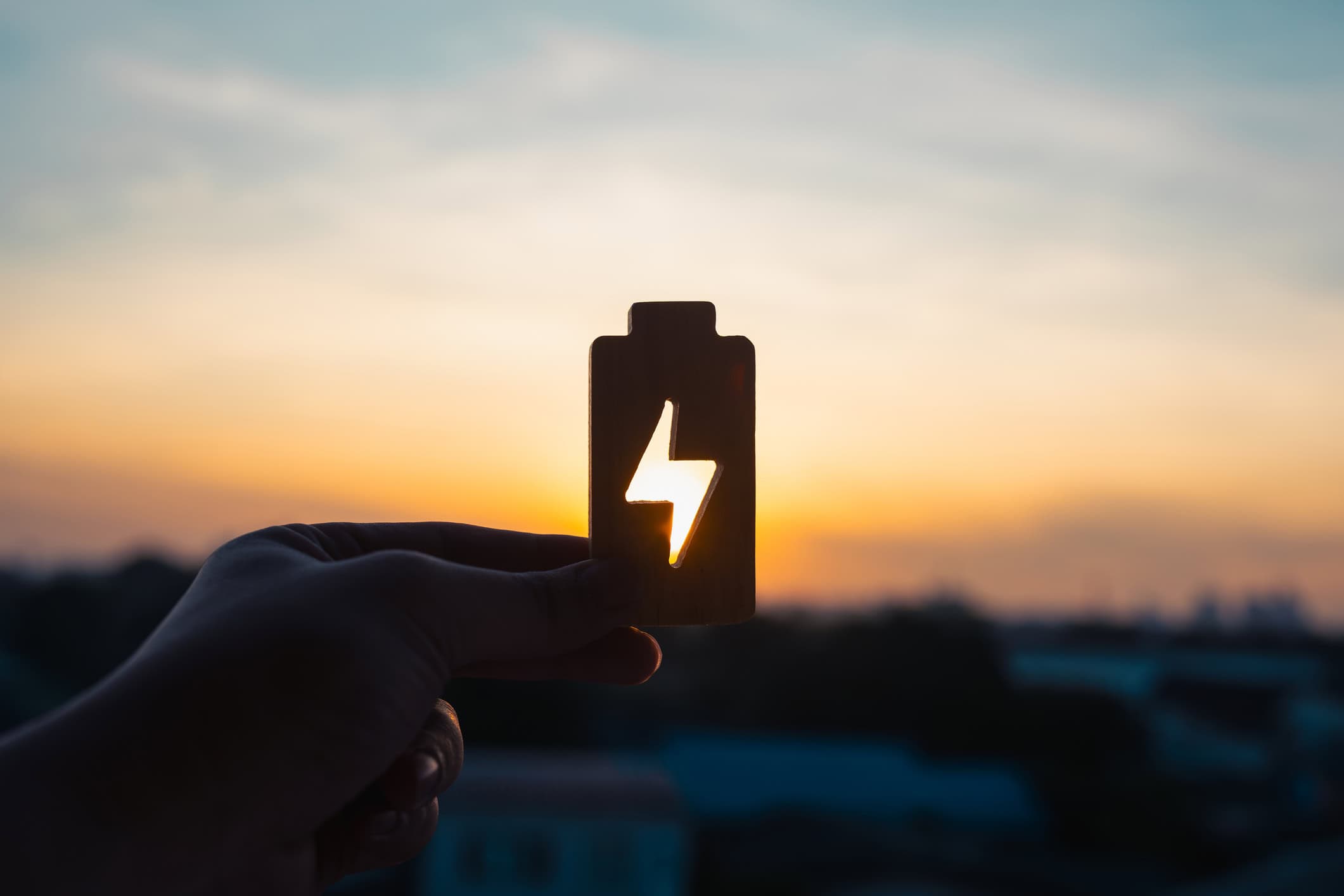 Close-up of a hand at sunset holding up an object resembling a battery with a hole in it.